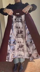 Tapado largo color borgoña, confeccionado en mezcla de lana y cashmere, de corte recto, sin botones frontales ni cruce. Presenta puños cruzados con botones dorados y forro con estampado floral.