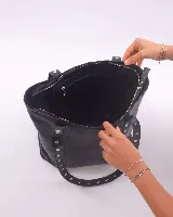 Bolso tote negro de cuero con tachas plateadas en las tiras. Tiene cierre superior, bolsillo interior y llavero.