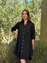 Vestido camisero blanco de lino, con cuello camisero, manga larga con botón para recoger, cierre frontal con botones de nácar, bolsillo en el pecho y diseño asimétrico más largo en la parte trasera.