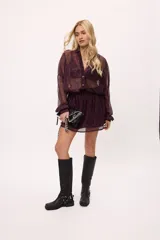 Vestido corto color borgoña con textura brillante, estilo camisero con botones y mangas largas. Tiene elástico en la cintura y es de corte suelto.