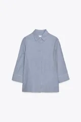 Camisa de cuello solapa y manga tres cuartos con puño ancho. Tiene aberturas laterales en el bajo y cierre frontal con botones ocultos.
