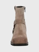 Bota corta de cuero color taupe, con caña de 14 cm, taco cuadrado de 6 cm y punta cuadrada. Presenta una correa con hebilla metálica alrededor del tobillo y cierre lateral.