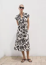 Vestido midi de manga corta con cuello camisero y cierre de botones frontal. Presenta un estampado floral grande en blanco y negro, y un cinturón ajustable a juego.