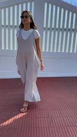 Mono largo de lino color beige, con breteles finos ajustables que se atan en la espalda, corte holgado y bolsillos laterales.