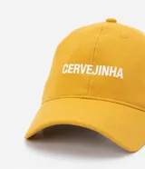 Gorra de sarga color mostaza con ala curva, bordado frontal con la palabra "cervejinha" en blanco y ajuste trasero con hebilla metálica.