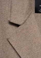 Abrigo largo color marrón claro con doble botonadura, cuello con solapa, hombros caídos y bolsillos laterales.