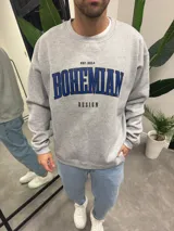 Buzo gris de algodón con cuello redondo y puños acanalados. Estampado frontal con la inscripción "Bohemian Design" en azul y "Est. 2014" en negro.