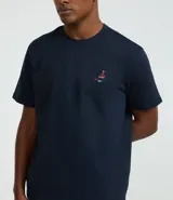 Remera de hombre color azul marino, corte regular, cuello redondo y manga corta. Presenta un pequeño bordado multicolor en el pecho que simula un barco y peces.