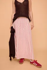 Pollera larga color crudo con rayas verticales rojas, de corte en línea A, con elástico en la cintura y largo hasta los tobillos.