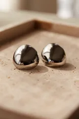 Aros tipo botón de acero quirúrgico hipoalergénico, con forma redondeada irregular y acabado brillante.