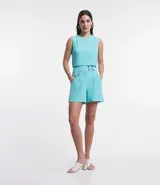 Blusa sin mangas color celeste, de crepé, con cuello redondo, pliegues en uno de los hombros y cierre trasero por cremallera con detalle de aro en el tirador.