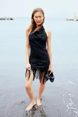 Vestido corto negro con cuello halter y espalda descubierta. Presenta bordados florales a tono y terminación con flecos.