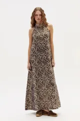 Vestido largo con estampado abstracto en tonos marrones y beige, cuello halter y corte en línea A. Confeccionado en lino 100% natural con terminación metalizada.
