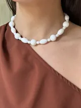 Collar corto de cuentas blancas de diferentes formas y tamaños, unidas por un hilo transparente.