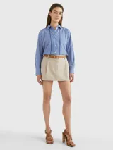 Camisa de manga larga a rayas verticales azules y blancas, con cuello inglés y corte amplio. Presenta detalles distintivos de la marca Tommy Hilfiger y logo bordado en el puño.