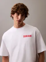 Remera blanca de algodón con cuello redondo, mangas cortas y logo de Calvin Klein Jeans estampado verticalmente en color rojo en el pecho.