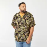 Camisa de manga corta con estampado de hojas tropicales en tonos verdes y marrones sobre fondo negro. Tiene cuello clásico, corte recto y cierre frontal con botones.