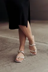 Sandalias negras de cuero con tira ancha sobre el empeine y tira entre los dedos, ambas adornadas con apliques metálicos plateados.