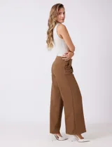 Pantalón sastrero color marrón, de tiro alto y corte recto, con un largo al tobillo. Presenta pretina limpia con cierre interno, bolsillos funcionales en la delantera y plisado que aporta volumen. La trasera tiene bolsillos ojal simulados.