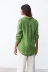 Camisa verde de lino con cuello clásico, cierre frontal con botones, mangas largas con trabilla para enrollar y dos bolsillos con solapa en el pecho.