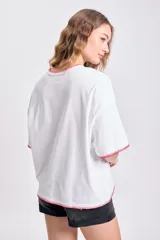 Remera blanca de corte holgado con cuello redondo y mangas cortas, terminaciones con pespunte rojo.