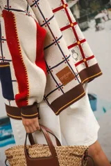 Cardigan oversized de tejido jacquard color crema con diseño de cuadrados en marrón y detalles bordados. Tiene cuello en V, cierre con botones, mangas largas y bolsillos frontales.