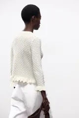 Chaqueta de punto amarilla con cuello redondo, manga larga y cierre frontal con botones. Detalle de volantes en los bordes.