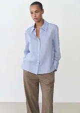 Camisa celeste con rayas verticales finas, de tejido fluido, manga larga abotonada, cuello camisero y corte recto.