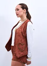 Chaleco marrón de gamuza sintética con apliques de flores y tachas doradas.