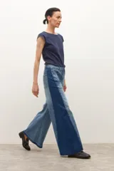 Pantalón de jean tiro alto, estilo wide leg, con paneles de denim en dos tonos de azul (claro y oscuro) cosidos verticalmente. Presenta un ruedo deshilachado.