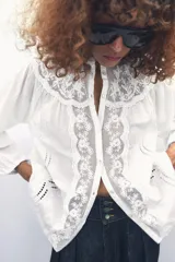 Camisa blanca de cuello redondo y manga larga con bordados combinados a tono y cierre frontal con botones.