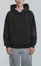 Hoodie negro de corte oversize con capucha, bolsillo tipo canguro y detalle de bolsillo con cierre en la manga izquierda.