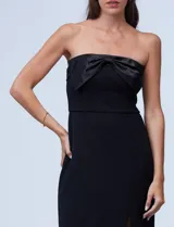 Vestido de fiesta corto strapless, color negro, confeccionado en crepe. Presenta escote recto con aplique de moño en satén y tajo en la parte delantera.
