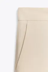Pantalón de vestir color beige, de tiro alto, con cintura elástica en la parte trasera, bolsillos delanteros y falsos bolsillos de vivo en la parte trasera.