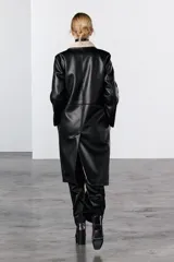 Abrigo largo de Zara Woman Collection, confeccionado en tejido efecto piel color negro. Tiene cuello solapa, manga larga, bolsillos laterales ocultos y forro interior de borreguillo color beige. El cierre es cruzado con botones.