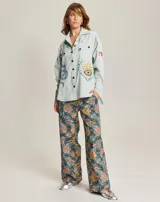 Camisa celeste de denim con bordados de motivos esotéricos, cuello abotonado, mangas largas con puños y dobladillo redondeado.