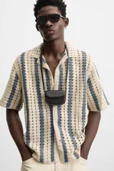 Camisa de crochet color beige con rayas verticales azules, cuello bowling, manga corta y cierre frontal con botones.