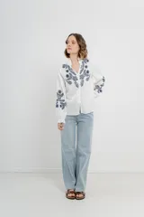 Camisa de manga larga en algodón liviano, color azul marino, con bordados florales en contraste en el frente y mangas. Cuello mao con terminación en ondas y puños fruncidos.