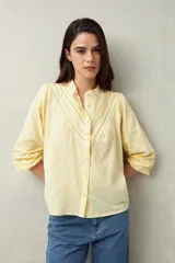 Camisa amarilla de algodón con cuello mao, mangas largas abullonadas con puños abotonados y calados centrales.