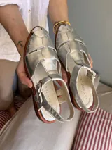 Sandalias plateadas de cuero con diseño tipo pescador, suela plana y hebilla lateral.