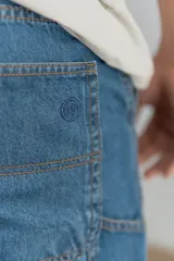 Bermuda de jean azul con bolsillos laterales y traseros, y bolsillo adicional en la pierna derecha.