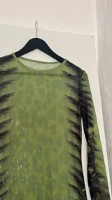 Vestido midi ajustado de microtul verde con estampado abstracto en tonos oscuros. De mangas largas y cuello redondo, es una prenda transparente y elástica.