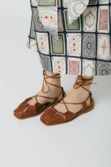 Sandalias bajas de cuero color marrón con tiras finas que se atan al tobillo.