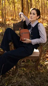 Bandolera de cuero sintético en color marrón claro con apertura superior de cierre. Presenta un bolsillo frontal con cierre y una correa de galón ajustable y desmontable con diseño a rayas. El interior incluye un bolsillo de fácil acceso.