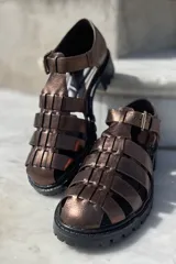 Sandalias de cuero color cobre con diseño de tiras entrecruzadas, hebilla lateral y suela track color negro.