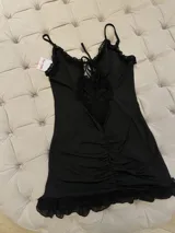 Minivestido negro con breteles finos, escote pronunciado con abertura y volados de tul transparente.