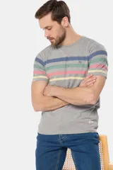 Remera de manga corta color gris jaspeado con cuello redondo y un patrón de rayas horizontales anchas en tonos pastel (azul, verde menta, rosado y amarillo). Presenta un pequeño logo bordado en el pecho.