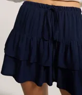 Short pollera de viscosa color azul marino, con cintura elástica y lazo ajustable, con diseño de volados superpuestos.