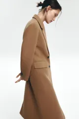 Abrigo largo color camel de Zara Woman Collection, confeccionado en hilatura con lana. Tiene cuello solapa con muescas, manga larga, falsos bolsillos delanteros, forro interior a contraste y cierre frontal con botones.