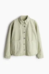 Sobrecamisa verde claro de sarga de algodón con cuello, botones adelante y canesú adelante y atrás. Modelo de hombros caídos con puños abotonados, bolsillos parche adelante y bajo levemente redondeado.